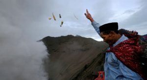 A Hindu worshipper throws offerings into the volcanic crater of Mount Bromo as smoke and ash rise from the volcano during the Kasada ceremony in Probolinggo, Indonesia